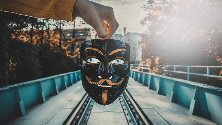 Eine Hand hält eine Maske in die Kamera.
