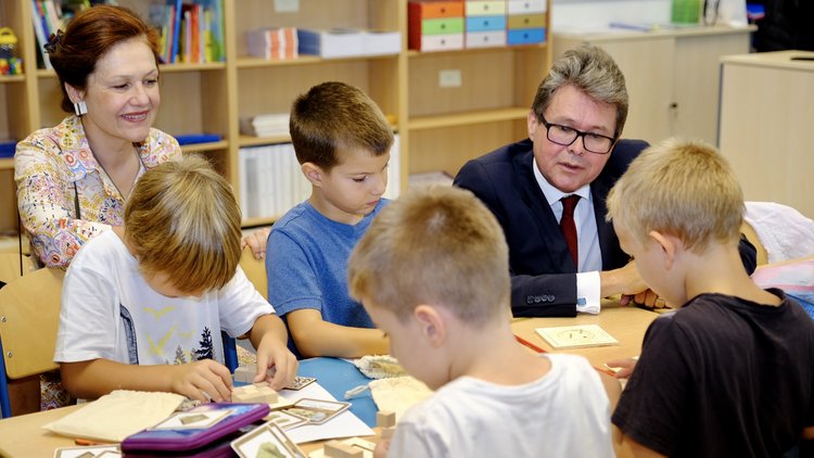 Bildungsminister Martin Polaschek und PH Wien-Rektorin Barbara Herzog-Punzenberger sehen Volksschulkindern über die Schulter, die den digi.case ausprobieren.