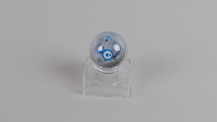 Der Sphero Mini Roboter auf einer transparenten Halterung vor grauem Hintergrund.