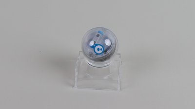 Der Sphero Mini Roboter auf einer transparenten Halterung vor grauem Hintergrund.