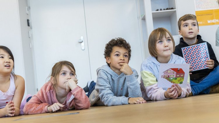 Eine Reihe von Kindern sitzt und liegt nebeneinander am Boden.