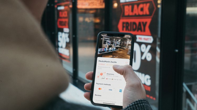 Person mit Handy vor einem Black-Friday-Poster