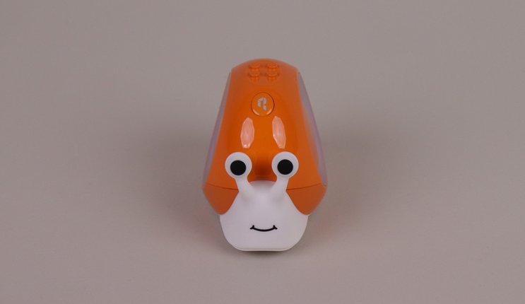 Der Smart-Snail-Roboter steht vor grauem Hintergrund. Die Schnecke hat einen weißen Körper mit großen, runden Augen und ein oranges Haus.