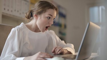 Eine junge Frau mit schockiertem Gesichtsausdruck schaut auf einen Laptop-Bildschirm.