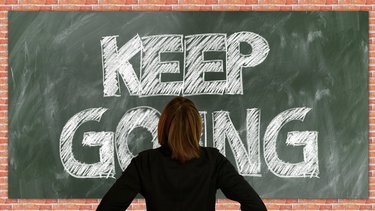 Eine Person von hinten vor einer Schultafel, auf der "Keep going" steht