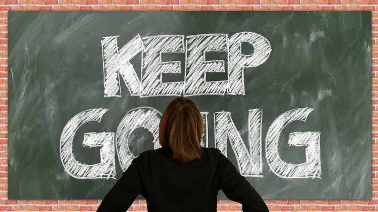 Eine Person von hinten vor einer Schultafel, auf der "Keep going" steht