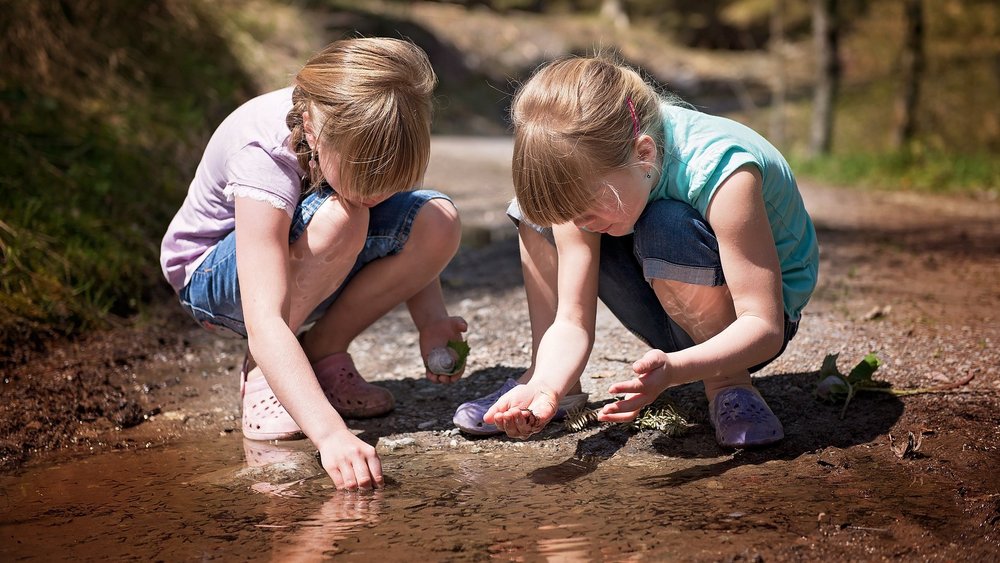 Zwei Mädchen hocken am Wasserrand und untersuchen etwas.