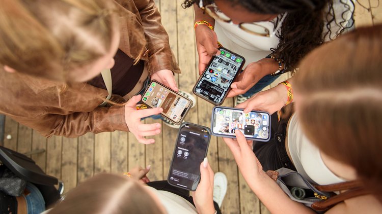 Vogelperspektive auf eine Gruppe Jugendliche die in einer Runde stehen, alle haben Smartphones in der Hand.