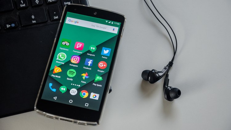 Ein Smartphone liegt auf einem Laptop, daneben liegt ein Paar Kopfhörer.