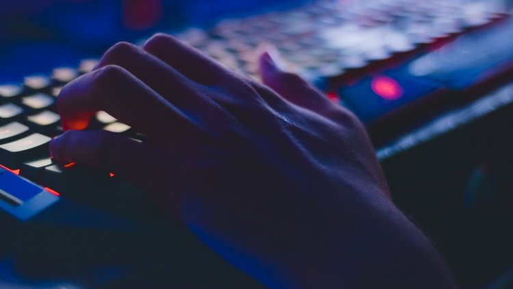 Eine Hand liegt in für Computerspiele typischer Haltung auf einer beleuchteten Tastatur.