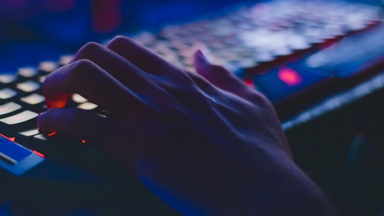 Eine Hand liegt in für Computerspiele typischer Haltung auf einer beleuchteten Tastatur.