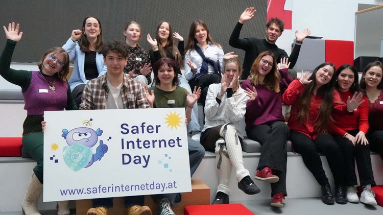 Auf dem Bild sind Schüler:innen auf Treppen sitzend zu sehen. Sie halten dabei ein Schild des "Safer Internet Days" in die Kamera und winken.