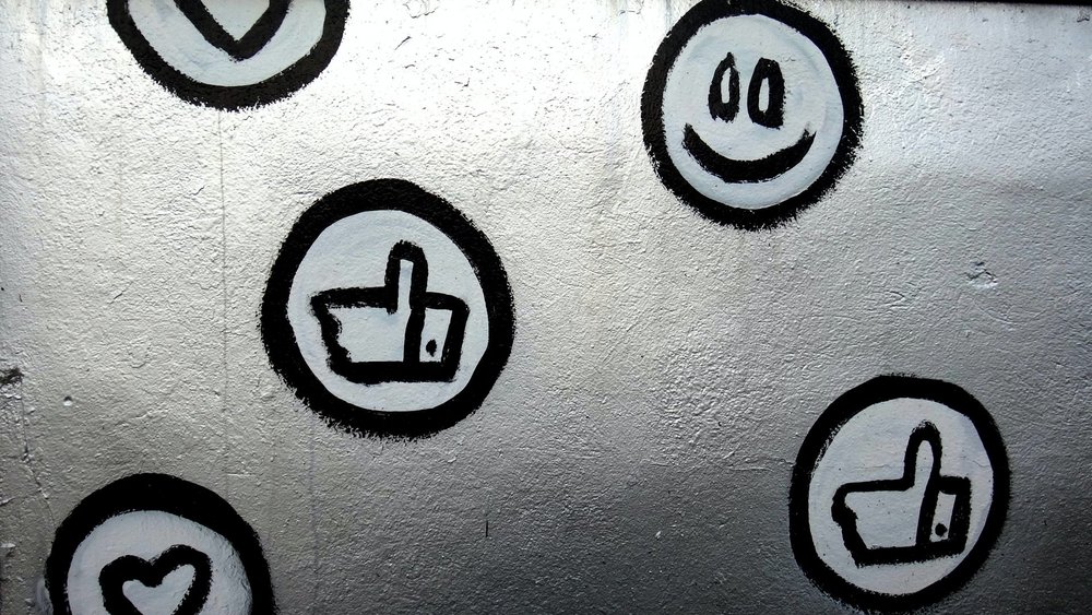 Bild von diversen kleinen Graffitis, die Emojis, Like-Buttons und Herzen darstellen.