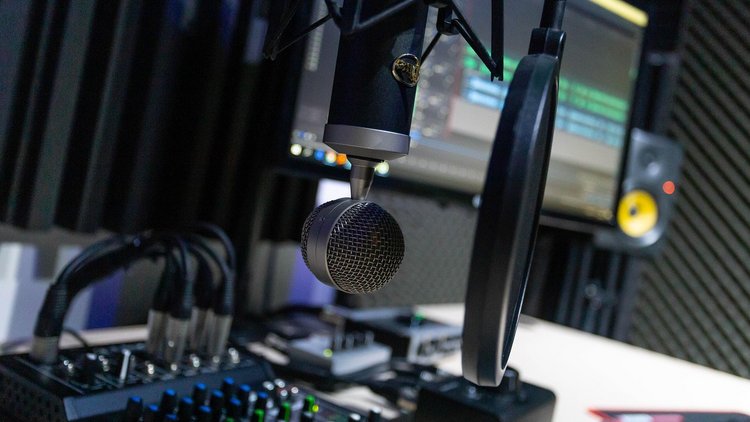 Im Bild ist ein Tonstudio zu sehen mit einem Mikrophon im Vordergrund