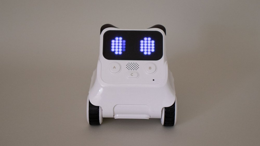 Ein kleiner, weißer Roboter mit Augen-förmiger Anzeige am LED-Display steht vor grauem Hintergrund.