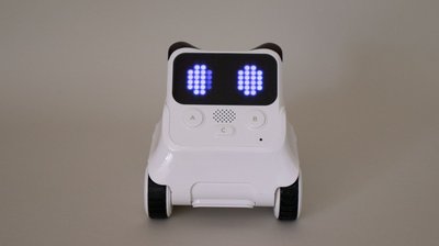 Ein kleiner, weißer Roboter mit Augen-förmiger Anzeige am LED-Display steht vor grauem Hintergrund.