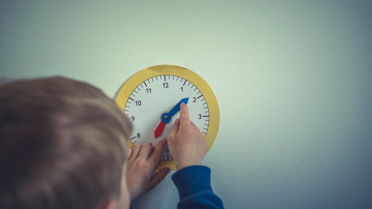 Kind mit Papieruhr zum Lernen der Uhrzeiten
