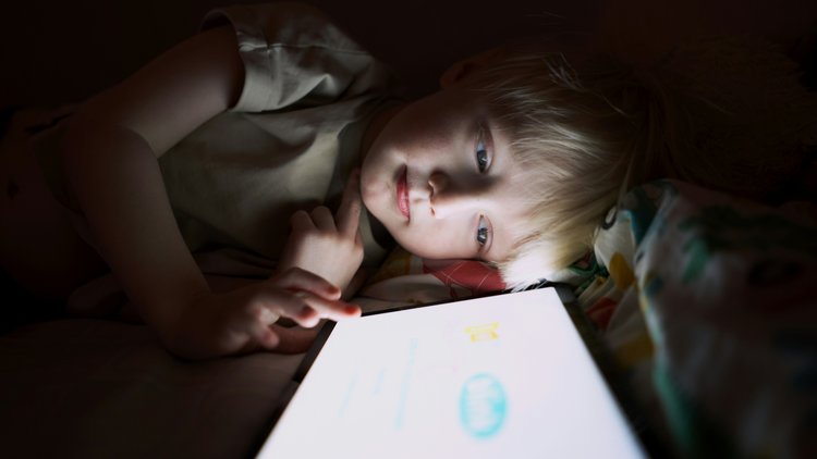 Ein Kind tippt im Liegen und im Dunkeln auf ein Tablet