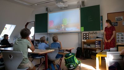 Eine Schulklasse: Die Schüler:innen sitzen an ihren Plätzen, am Beamer wird ein Stop Motion Film abgespielt.