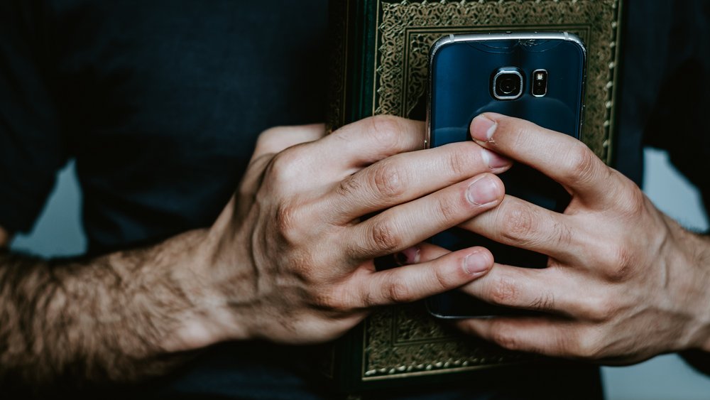 Zwei Hände, die ein religiöses Buch und ein Smartphone umklammert halten