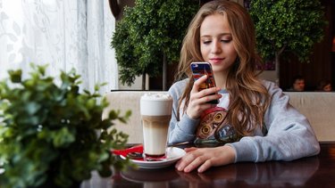 Junge Frau schaut neben Kaffee auf ihr Smartphone und lächelt