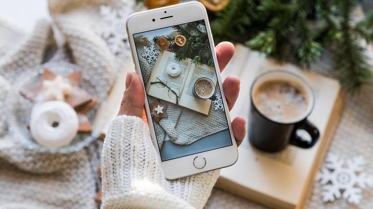 Eine Person hält ein Smartphone vor weihnachtlichen Motiven in die Höhe, am Bildschirm selbst sind auch weihnachtliche Motive zu sehen
