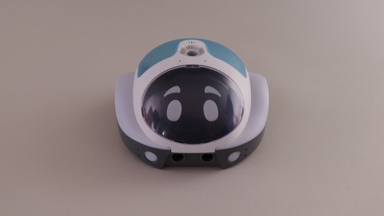 Ein weiß-blauer, rundlicher, flacher Roboter mit Augen und einem Loch in der Mitte des Roboters vor grauem Hintergrund.