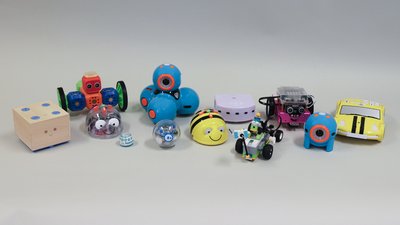 Verschiedene Lernroboter stehen aufgereiht nebeneinander vor grauem Hintergrund