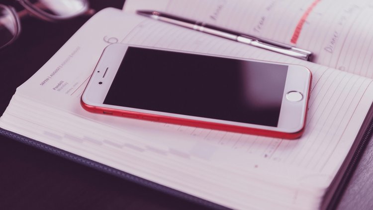 Ein Smartphone in rotem Rahmen liegt auf einem Taschenkalender