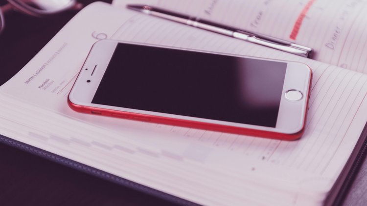 Ein Smartphone in rotem Rahmen liegt auf einem Taschenkalender