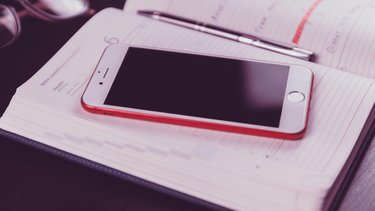 Ein Smartphone in rotem Rahmen liegt auf einem Taschenkalender