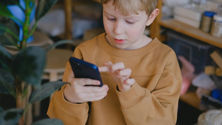 Ein Bub hält ein Smartphone in einer Hand, mit der einem Finger der anderen Hand berührt er den Display.
