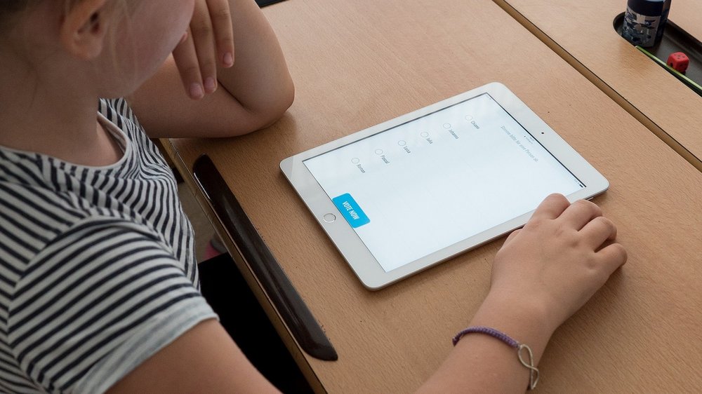 Eine Schülerin sitzt an ihrem Schul-Schreibtisch, vor ihr liegt ein Tablet mit einer Lernapp.