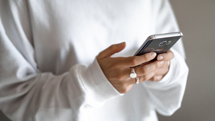 Nahaufnahme von zwei Händen, die ein Smartphone halten und darauf tippen.