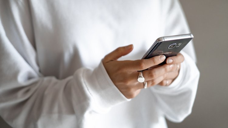 Nahaufnahme von zwei Händen, die ein Smartphone halten und darauf tippen.