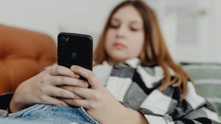 Eine Jugendliche liegt auf einer Couch mit einem Smartphone in der Hand.