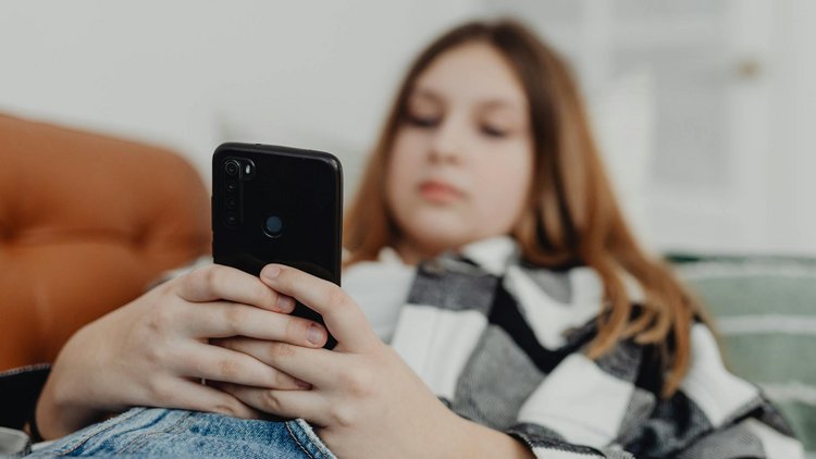 Eine Jugendliche liegt auf einer Couch mit einem Smartphone in der Hand.