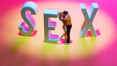 Zwei Figuren küssen sich zwischen den Buchstaben E und X, insgesamt ist das Wort SEX zu lesen