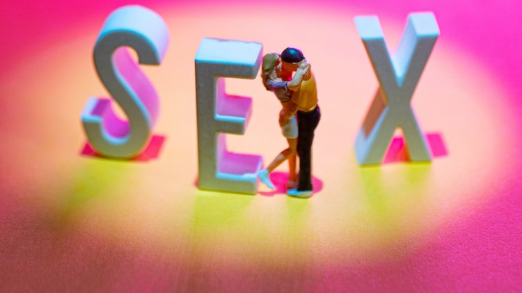Zwei Figuren küssen sich zwischen den Buchstaben E und X, insgesamt ist das Wort SEX zu lesen