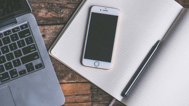 Links ist ein Laptop zu sehen, rechts ein Kalender mit einem Stift und einem Smartphone darauf