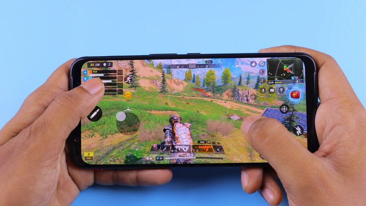 Nahaufnahme von zwei Händen, die ein Smartphone quer halten. Am Smartphone ist ein Shooter-Spiel geöffnet.