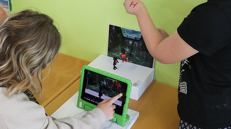 Es sind Kinder von hinten zu sehen, die gerade mit einem grün ummantelten Tablet einen Stop Motion Film produzieren
