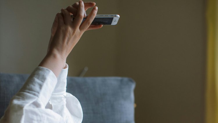 Zwei Hände einer liegenden Person halten ein Smartphone in die Höhe.