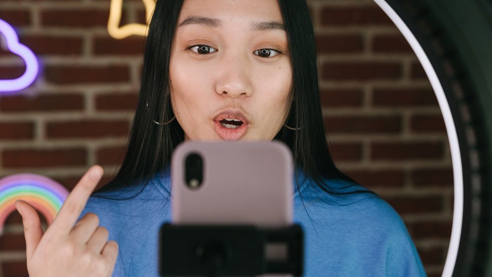Nahaufnahme einer jungen Frau die im Selfie-Modus in ihr Smartphone spricht.
