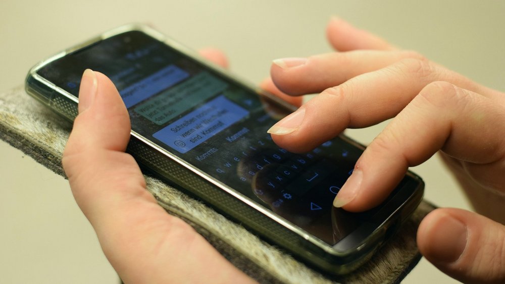 Zwei Hände halten ein Smartphone, am Bildschirm ist ein WhatsApp-Chat zu erkennen.