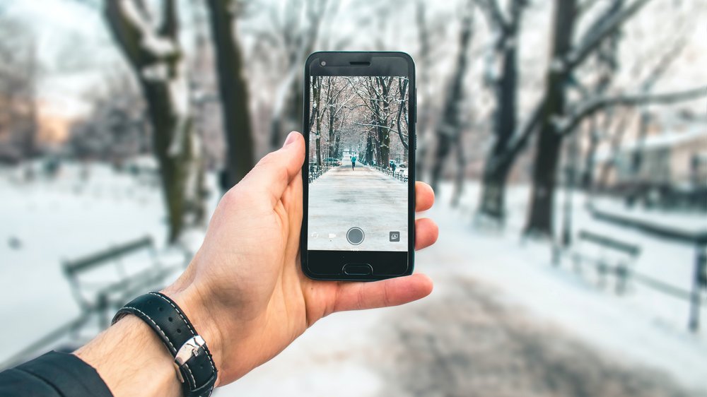 Eine Hand hält ein Smartphone in einer Winterlandschaft mit Jogger