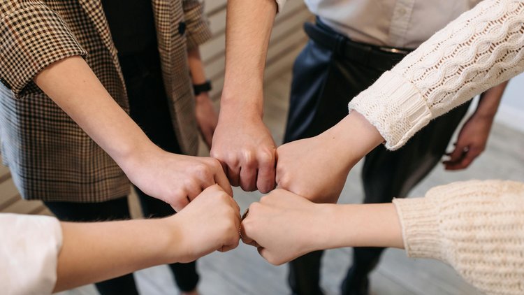 Die Hände von fünf verschiedenen Personen sind zu Fäusten geballt ausgestreckt und werden kreisförmig aneinander gehalten.