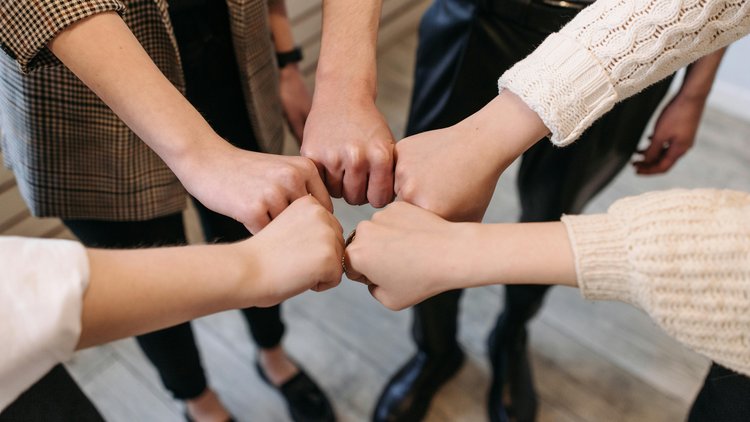 Die Hände von fünf verschiedenen Personen sind zu Fäusten geballt ausgestreckt und werden kreisförmig aneinander gehalten.