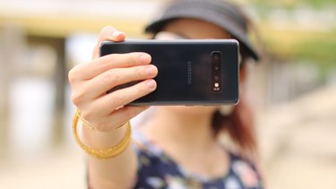 Eine Person hält ein Smartphone vor das eigene Gesicht und nimmt ein Foto (Selfie) von sich selbst auf. 