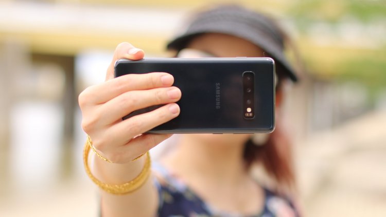 Eine Person hält ein Smartphone vor das eigene Gesicht und nimmt ein Foto (Selfie) von sich selbst auf. 